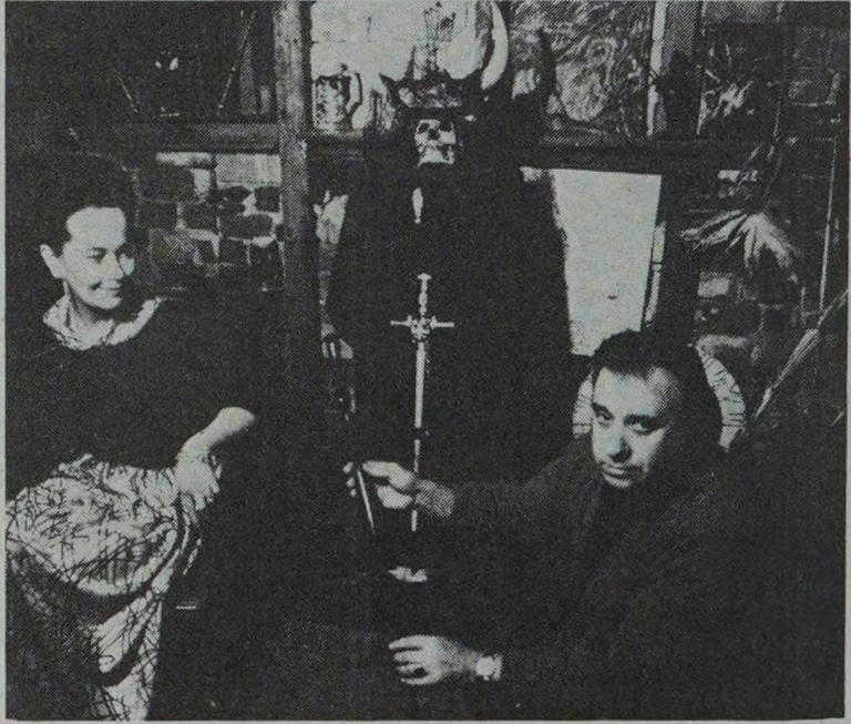 Vintage photo: two people sitting; one holds a sword, dark figure in the background.