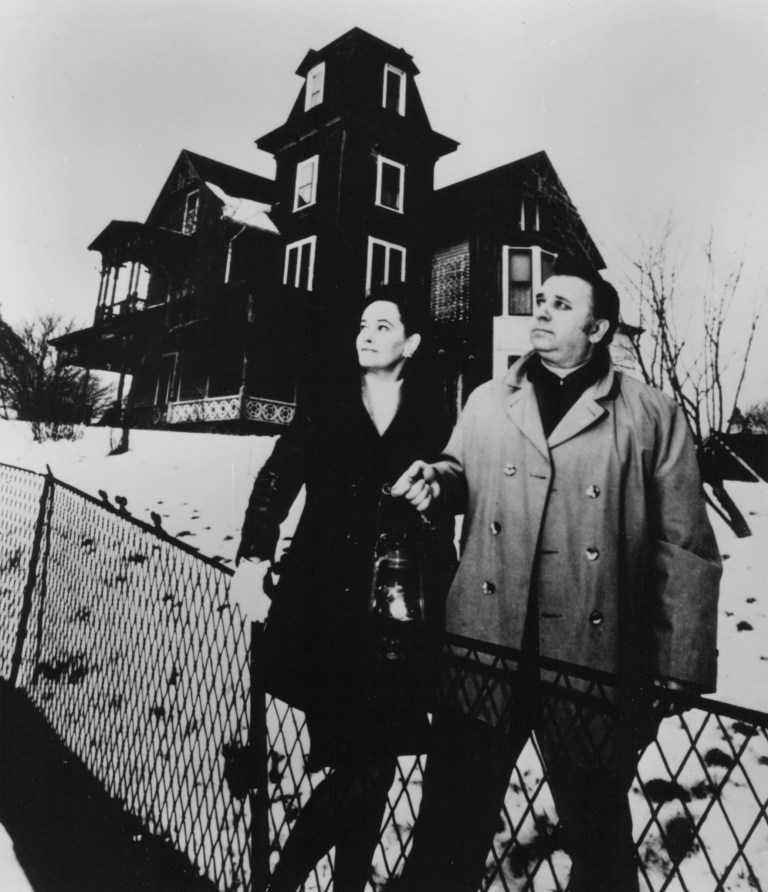 Two people with lantern near a spooky, dark house in snow.