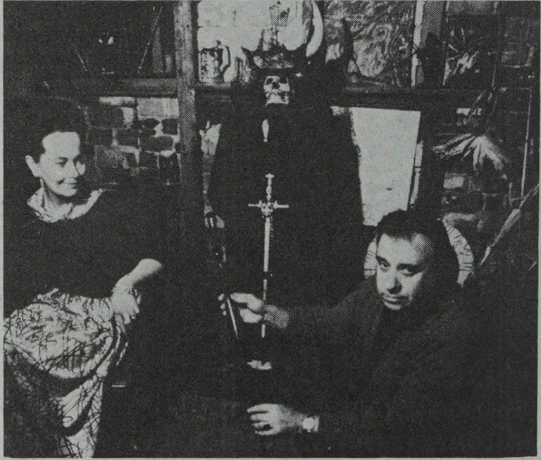 Vintage photo: two people sitting; one holds a sword, dark figure in the background.