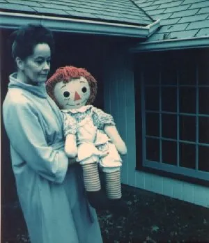 Person holding large Raggedy Ann doll outside a building.